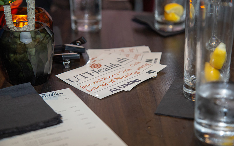 Close up view of table top with empty drinking glasses and centered focal point of UTHealth Houston Alumni name badges