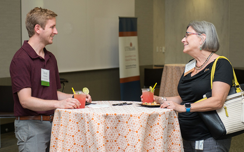 Man and woman standing at a standing table with food and pink drinks in front of them