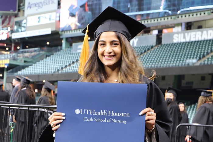 A new graduate holding up her degree that reads UTHealth Houston Cizik School of Nursing