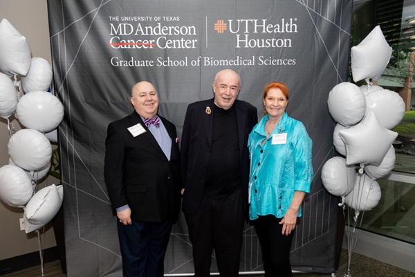 Three people standing in front of an MD Anderson Graduate School sign at an event