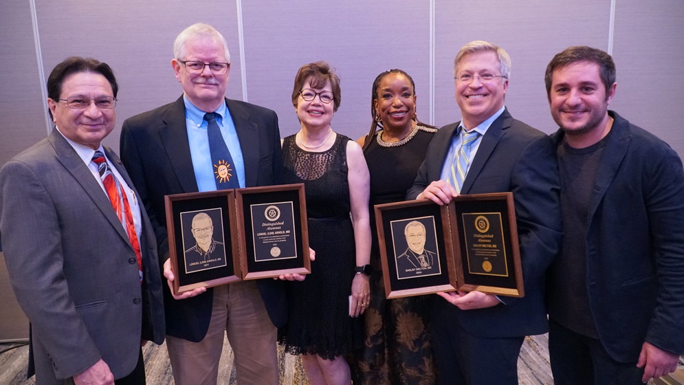 Two Distinguished Alumnus Awards winner holding their award and standing with a group of people