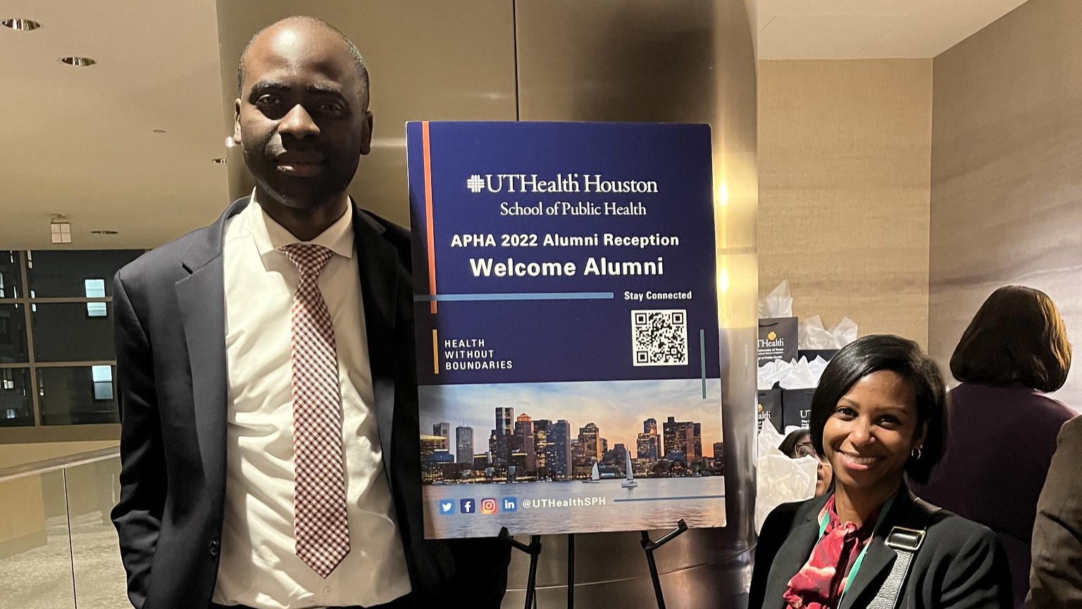 Two people standing in from of the APHA 2022 Alumni Reception weclome sign