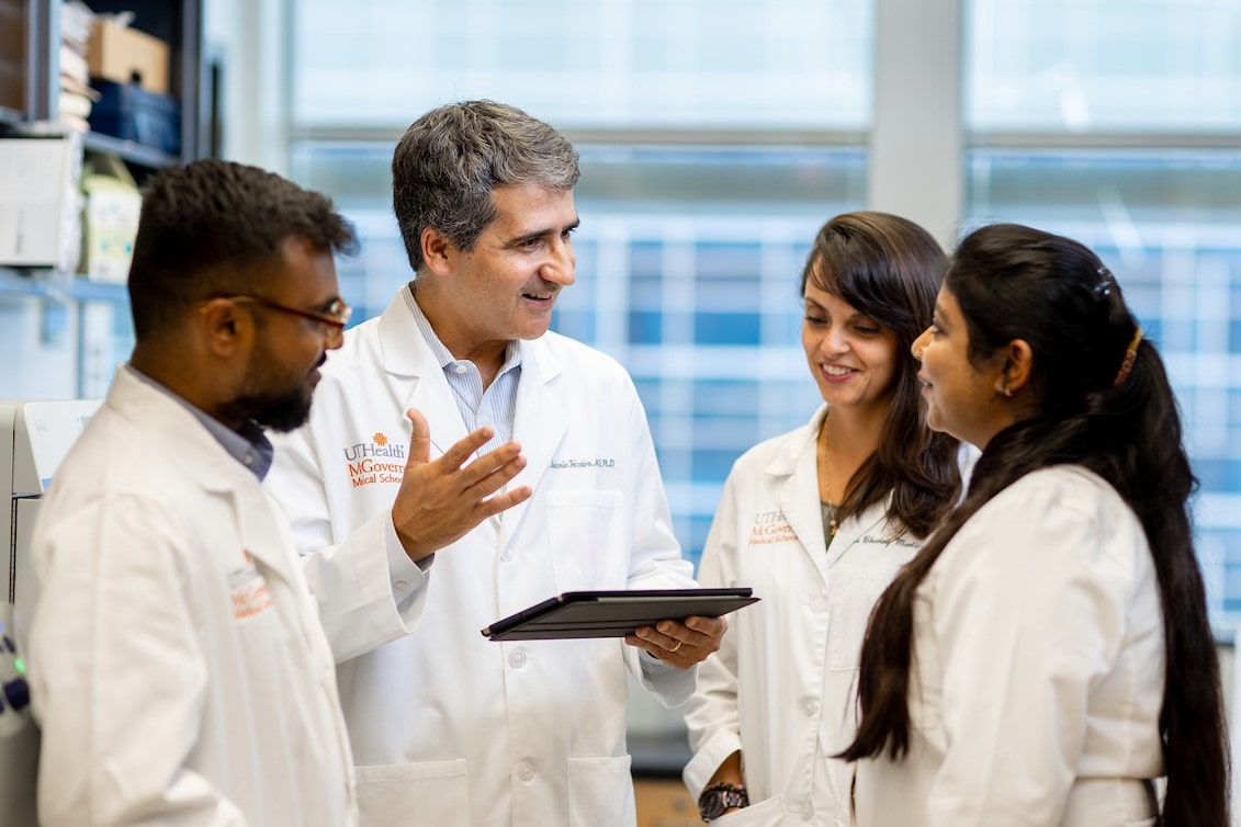 A group of faculty members wearing white coats and standing in a circle having a discussion