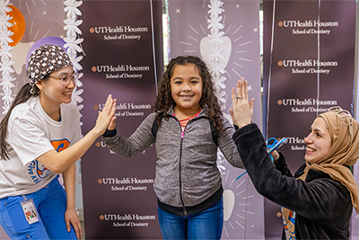 Posed image of young girl with arms raised standing between two medical students giving each a high five